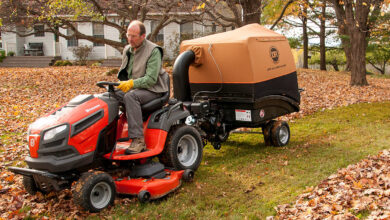 Person using a leaf vacuum to clean up fallen autumn leaves in a backyard