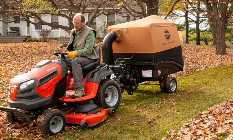 Person using a leaf vacuum to clean up fallen autumn leaves in a backyard